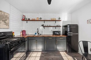 A modern kitchen with a gas stove, microwave, and Galanz refrigerator. There are wooden shelves above the sink and a map on the wall. - Cottage#6 - Spearfish Orchard Creek Cottages (Spearfish)