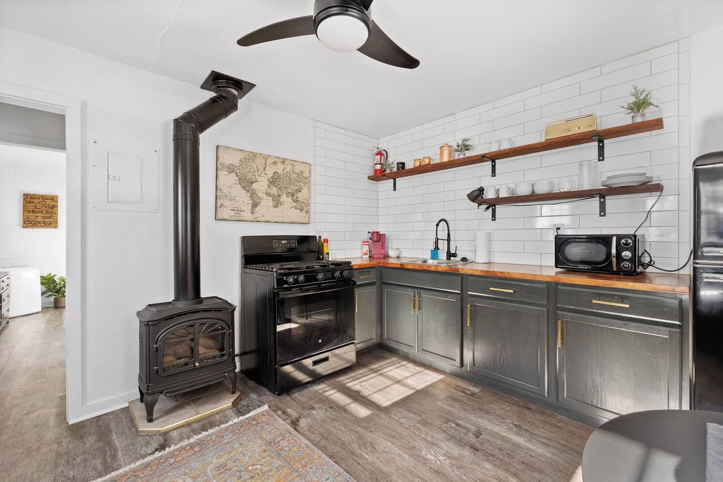 A modern kitchen with a wood-burning stove, stainless steel appliances, and a world map on the wall.