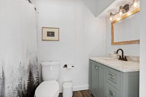 A bathroom with a toilet, sink, and mirror. - Cottage#6 - Spearfish Orchard Creek Cottages (Spearfish)