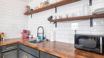 Een keuken met een roestvrijstalen spoelbak, houten planken, een zwarte magnetron en een witte betegelde achterwand.