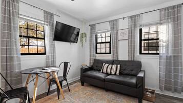 Ein modernes Wohnzimmer mit einem schwarzen Ledersofa, einem kleinen Tisch und einem an der Wand montierten Fernseher.