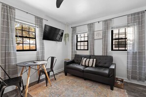 Een moderne woonkamer met een zwarte leren bank, een bijzettafeltje en een aan de muur bevestigde televisie.