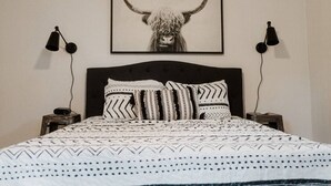 Ein Bett mit gemusterten Betttextilien, ein gerahmtes Kunstwerk mit einem gehörnten Tier und zwei Wandlampen.