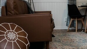 Ein Zimmer mit einem braunen Sofa, einem gemusterten Teppich, einer Lampe und einem gerahmten Bild an der Wand.