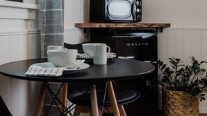 Eine kleine Küche mit Mikrowelle, Kaffeemaschine und Wasserkocher auf einer Holzablage. Ein runder Tisch mit Stühlen und ein Topfpflanze stehen daneben.