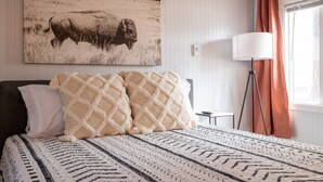 A bedroom with a bed, pillows, a lamp, a window with curtains, and a wall-mounted picture. - Cabin #11 - Spearfish Orchard Creek Cottages (Spearfish)
