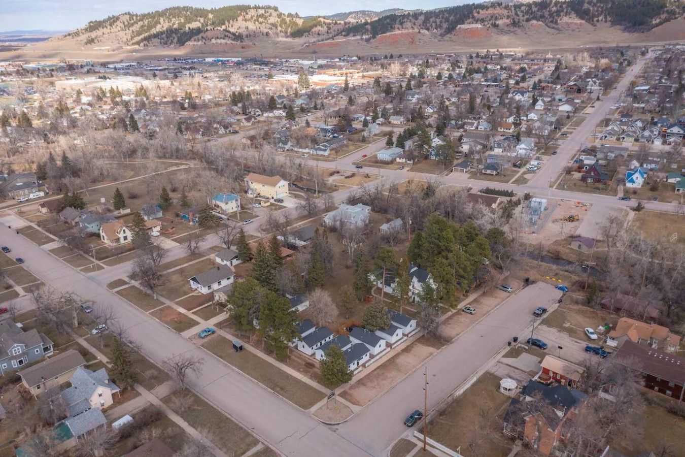 Vue aérienne d’un quartier résidentiel avec des maisons, des rues et un paysage vallonné en arrière-plan.