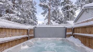 Ein Whirlpool, umgeben von schneebedeckten Bäumen und einem Holzzaun.