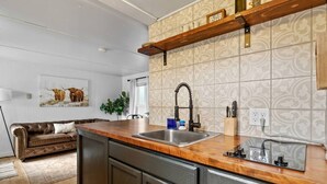 A kitchen with a wooden countertop, stainless steel sink, and a hanging shelf with a 'Hello' sign. - Cabin #11 - Spearfish Orchard Creek Cottages (Spearfish)