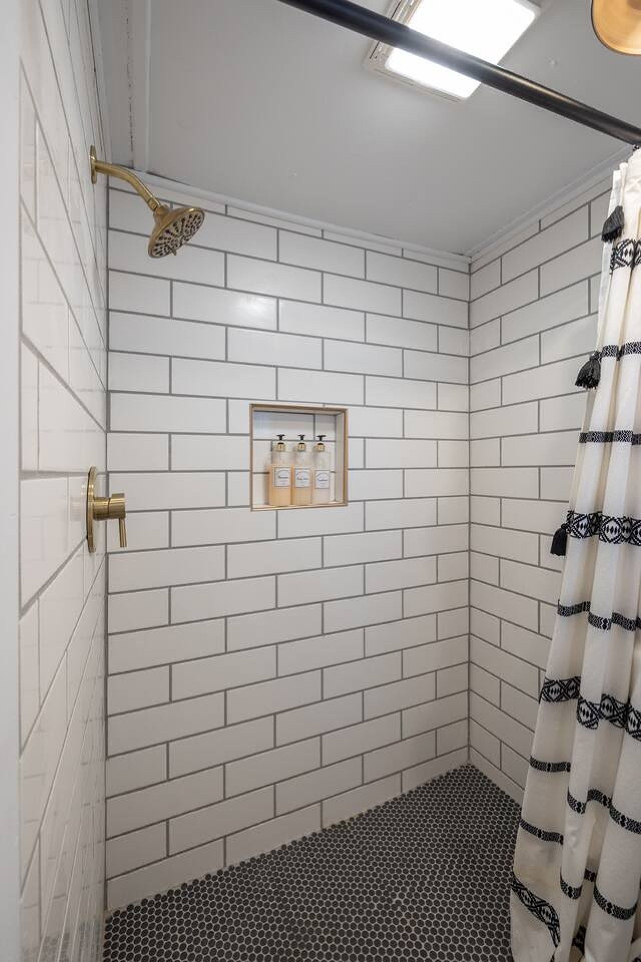 A shower with a gold showerhead, a framed soap dispenser, and a black and white patterned shower curtain.