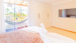 A bedroom with a bed, a TV, and a large window with a view of greenery outside. - IT32 Triplex 4 Suítes a 100m da Praia (Camaçari)