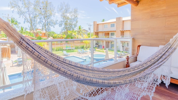 A hammock on a balcony overlooking a pool and a garden. - IT32 Triplex 4 Suítes a 100m da Praia (Camaçari)
