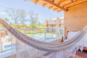 Un hamac sur un balcon donnant sur une piscine et un jardin.