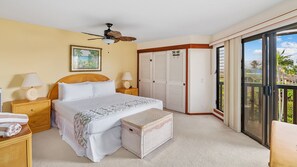 Une chambre avec un lit, des tables de chevet, un ventilateur de plafond, une fenêtre donnant sur un paysage agréable et une porte coulissante menant à un balcon.