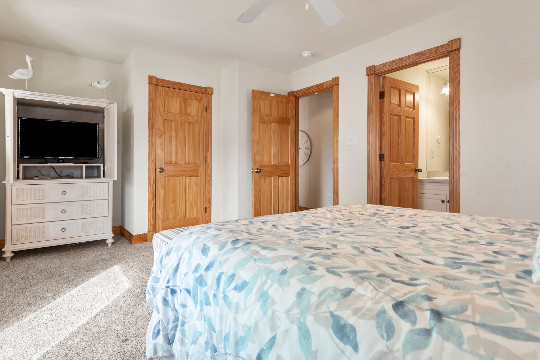 A bedroom with a bed, a dresser with a television, wooden doors, and a ceiling fan.