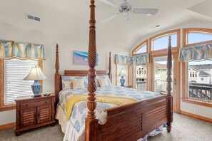 A bedroom with a four-poster bed, a ceiling fan, and large windows with curtains.