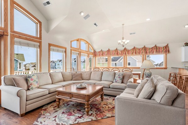 A spacious living room with a large sectional sofa, a coffee table, and a dining area with a chandelier.