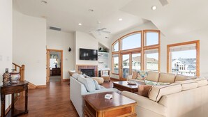 A spacious living room with a fireplace, large windows, and a high ceiling.