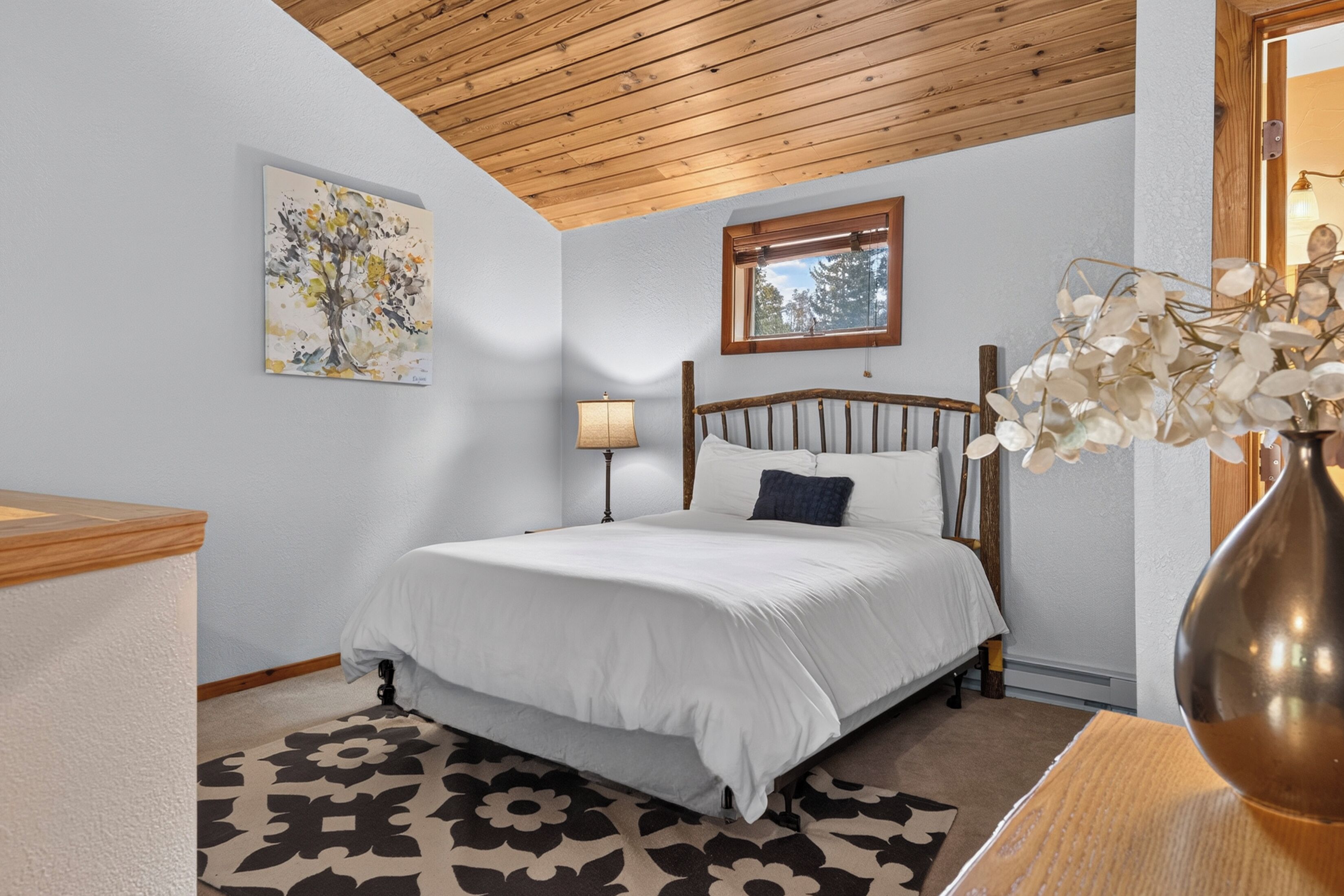 A bedroom with a bed, a window, a lamp, and a painting on the wall.