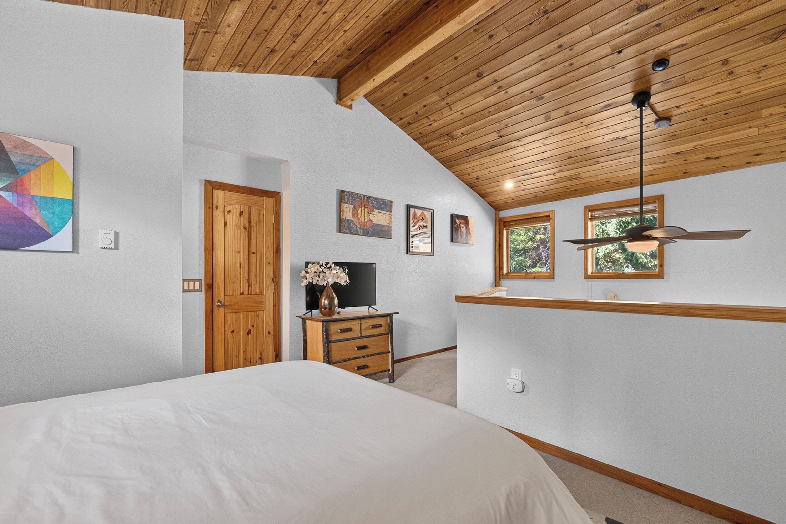 Una camera da letto con un letto, soffitto in legno, una cassettiera, un televisore e opere d'arte alle pareti.