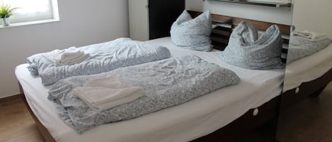 A neatly made bed with patterned bedding and pillows, a bedside table with a plant, and a window with natural light.