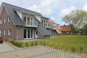 A two-story house with a sloped roof, a balcony, and a paved driveway. - Haus Seesturm (Dornum)