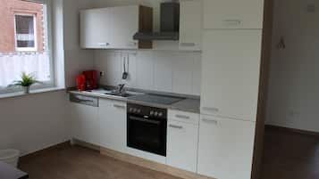Cuina moderna amb armaris blancs, forn integrat i finestra amb planta.