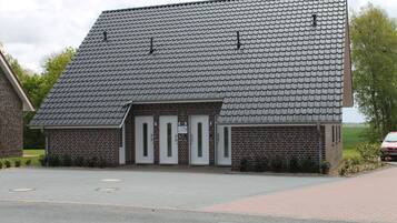 Ein Gebäude aus Backsteinen mit einem geneigten Dach, drei Eingängen und einer gepflasterten Auffahrt.