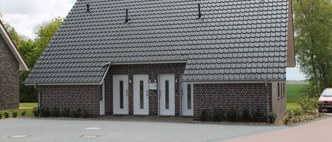En byggnad av tegel med ett sluttande tak, tre dörrar och en asfalterad uppfart.