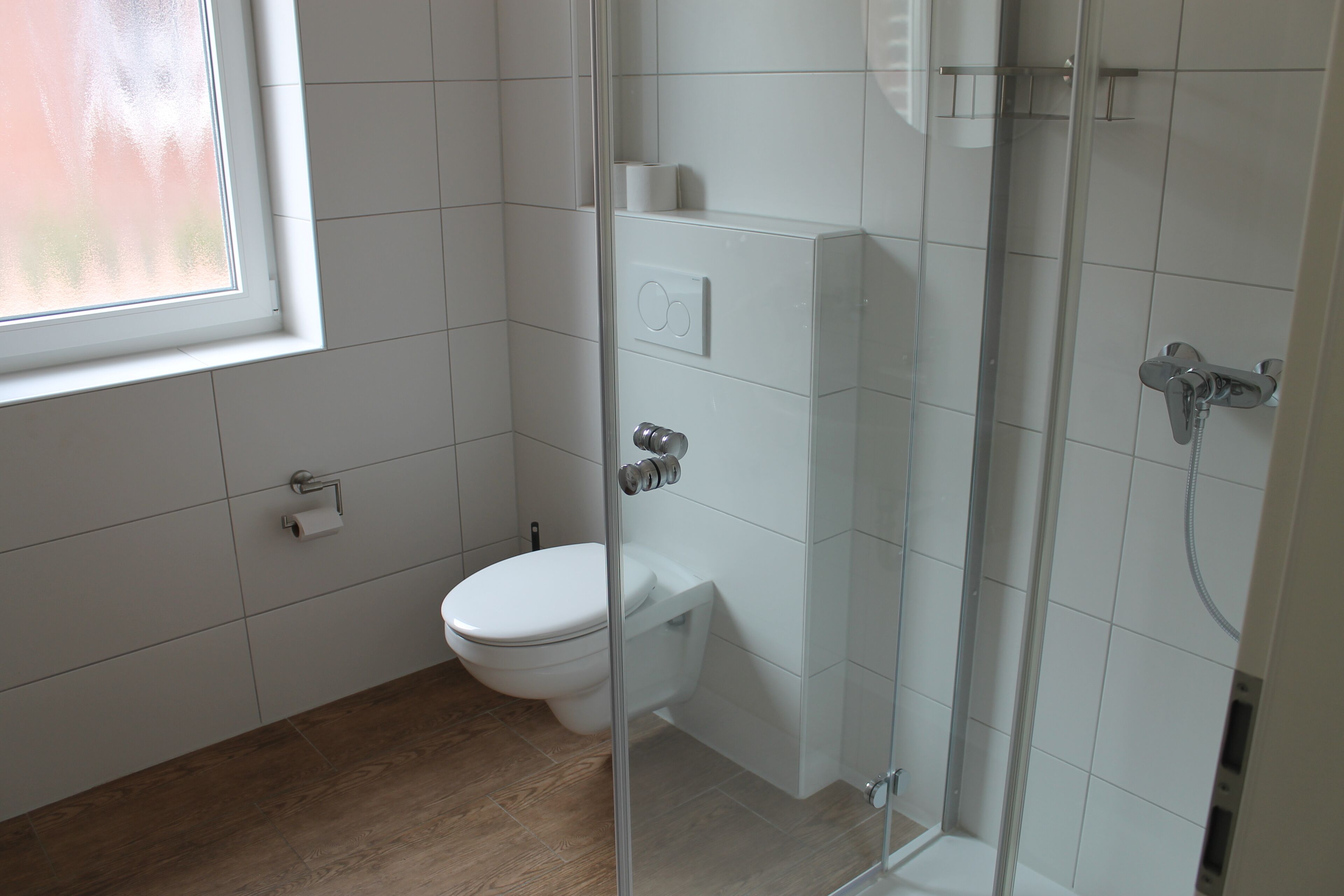 Een badkamer met toilet, een glazen douchecabine en een raam.