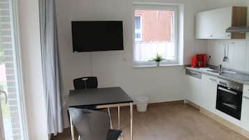 Cocina compacta con mesa de comedor, televisor montado en la pared, ventana con planta y horno empotrado.
