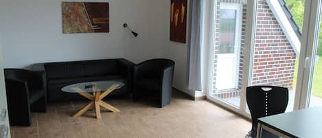 A modern living room with a black sofa, a round glass table, and a black chair.