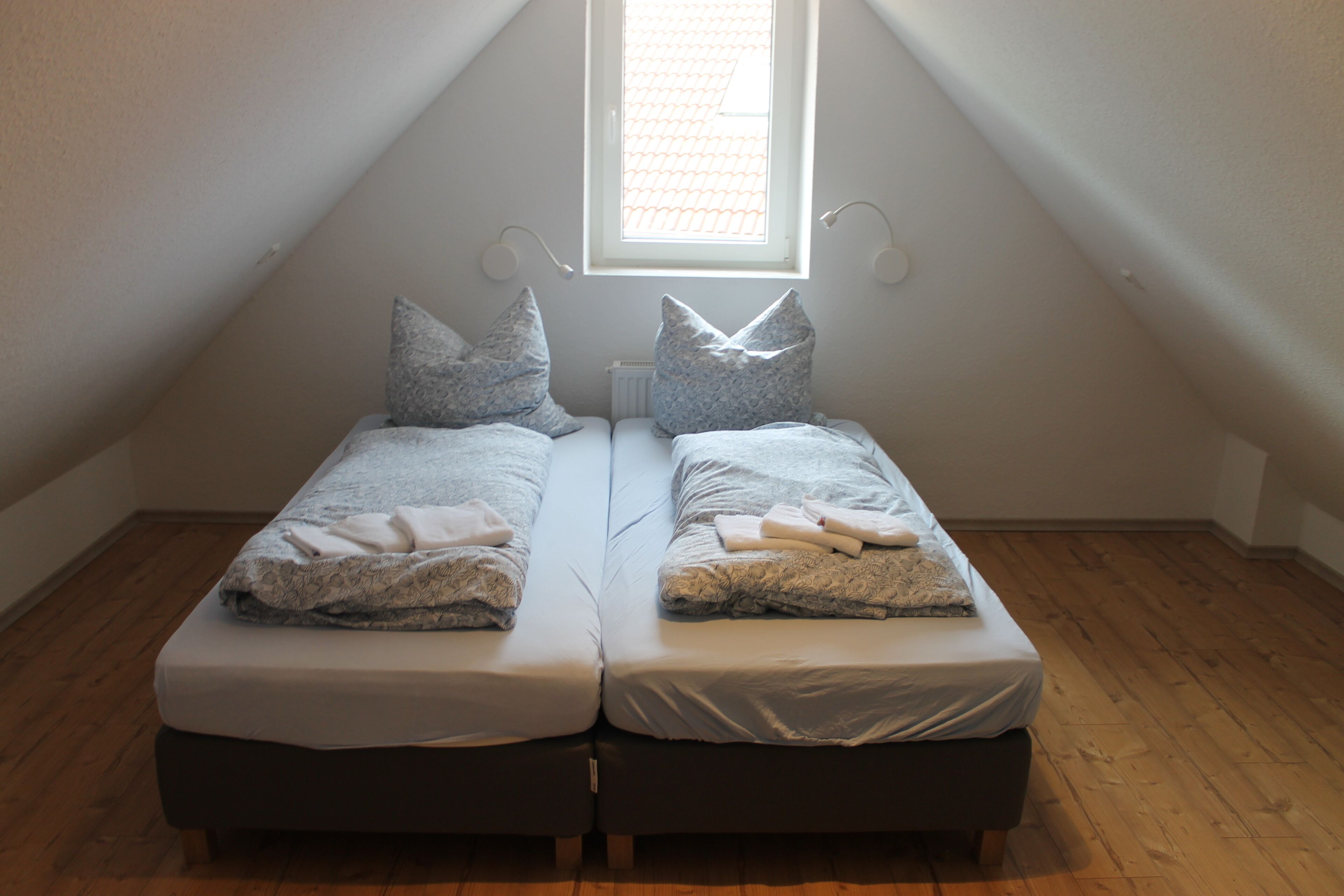A small, cozy room with two single beds, a window, and a sloped ceiling.