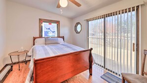 Un dormitorio con cama de madera, ventilador de techo, ventana con persianas y vistas al exterior.