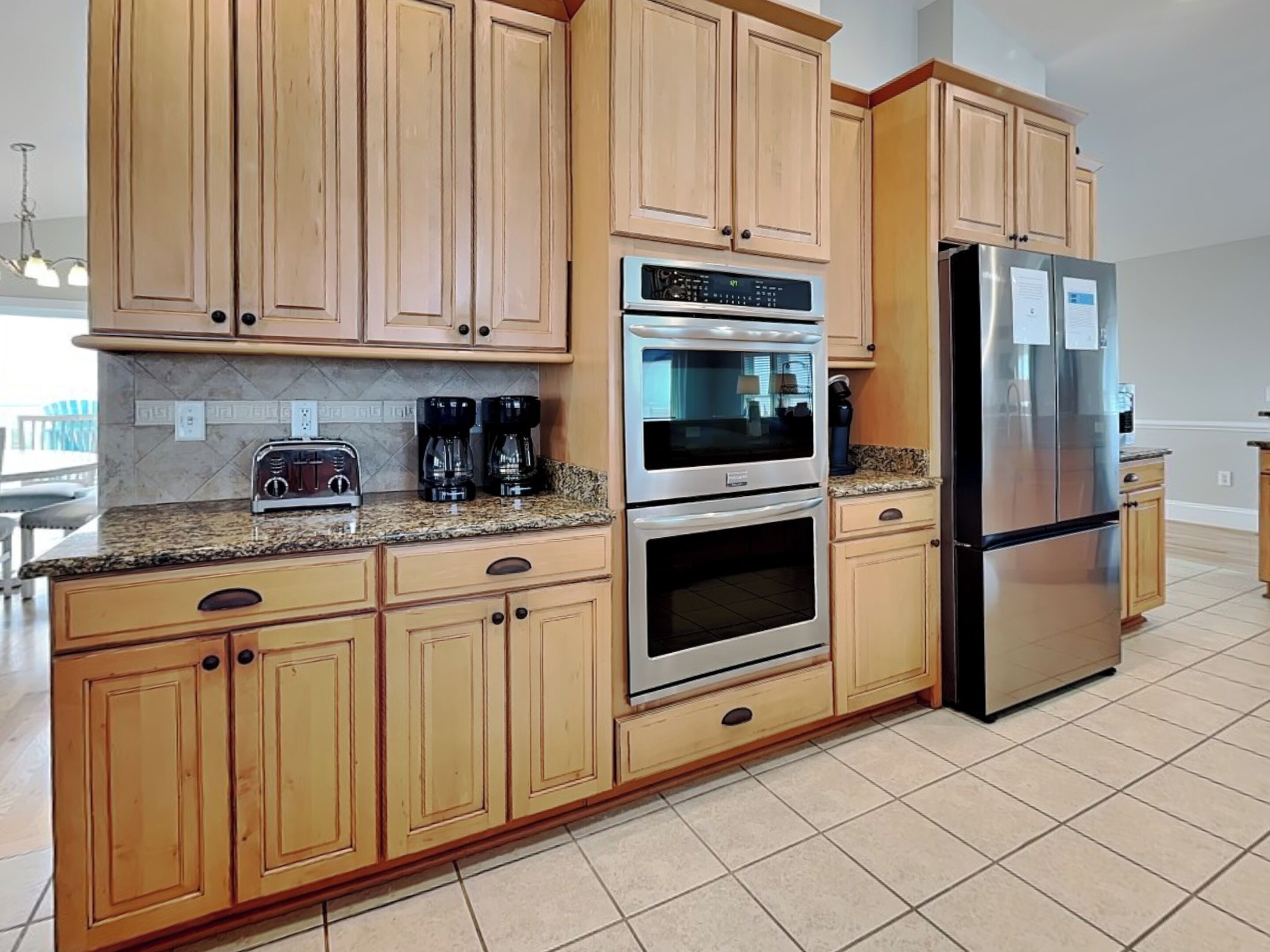 A modern kitchen with wooden cabinets, a stainless steel refrigerator, an oven, and a coffee maker.