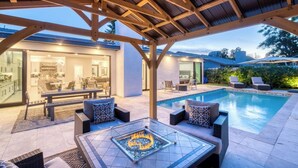Un espacio al aire libre techado con piscina, mobiliario y una chimenea.