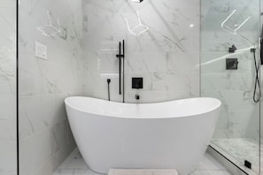 A modern bathroom with a freestanding bathtub, glass shower enclosure, and marble tiles.