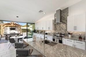 Uma cozinha moderna com armários brancos, bancadas de granito e eletrodomésticos de aço inoxidável.