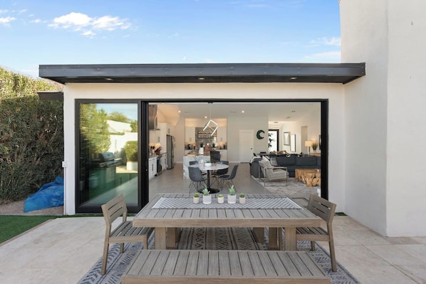 A modern house with an open-plan living area, a dining area with a table and chairs, and a kitchen visible through glass doors.