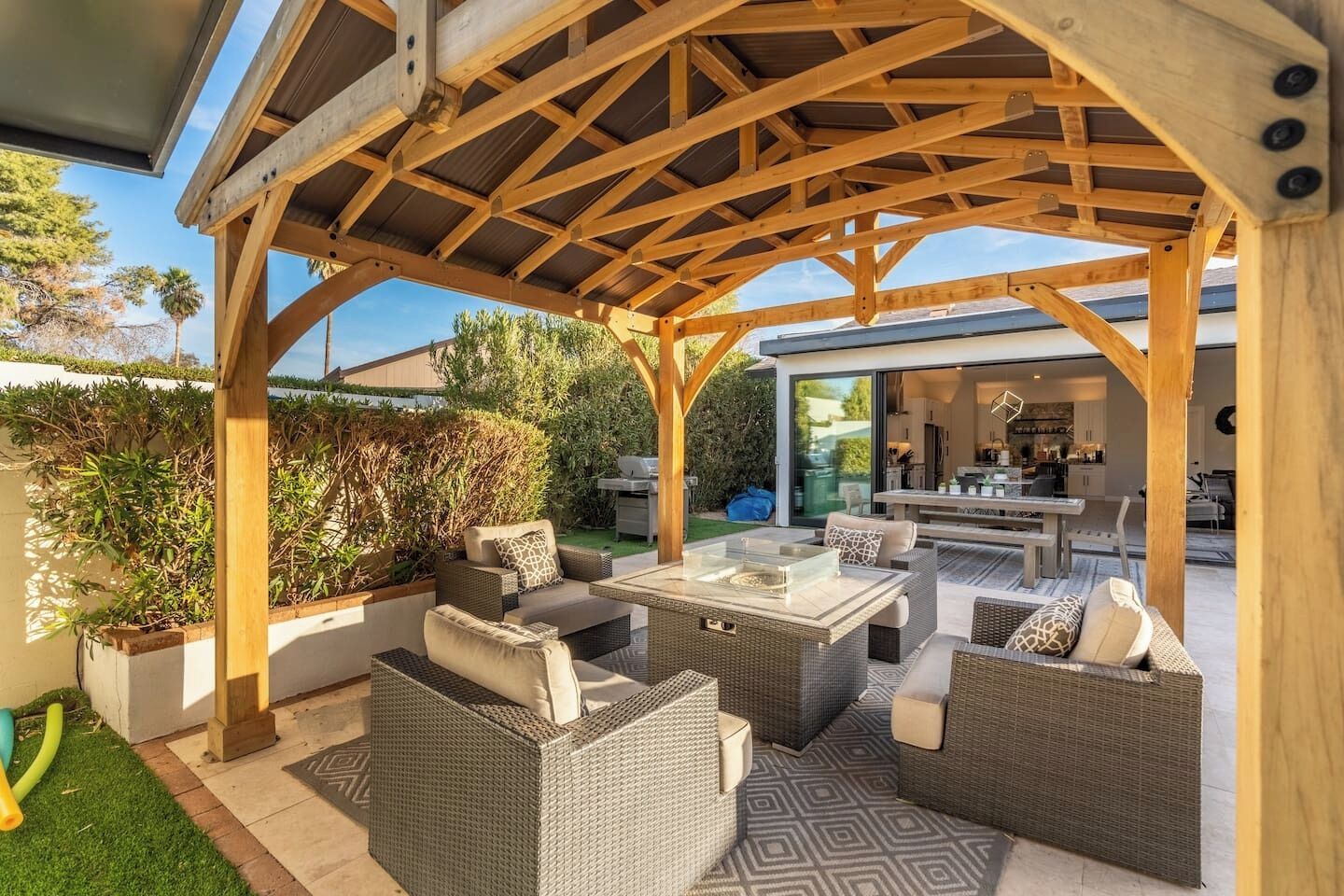 A covered outdoor patio with wicker furniture, a glass-top table, and a view of the house's interior.