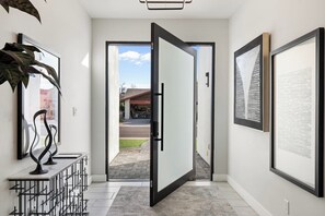 A hallway with a door leading outside, framed artwork on the walls, and a plant on the left.