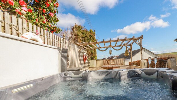 A hot tub area with a wooden pergola and a wooden fence with flowers.