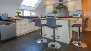 A modern kitchen with a skylight, stainless steel appliances, and a central island with bar stools.