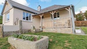 A two-story house with a stone foundation, a wooden porch, and a stone planter in the front yard.