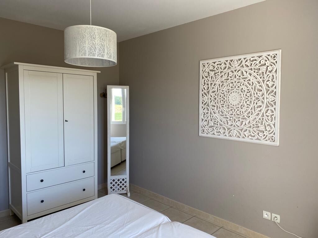 A bedroom with a bed, a wardrobe, a hanging light fixture, and a decorative wall panel.
