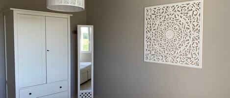 A bedroom with a bed, a wardrobe, a hanging light fixture, and a decorative wall panel.