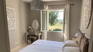 A bedroom with a large bed, a desk with a mirror, a window with curtains, and a view of the outdoors. - Spacious, bright villa. Charm, comfort and calm. Heated swimming pool. (Argilliers)