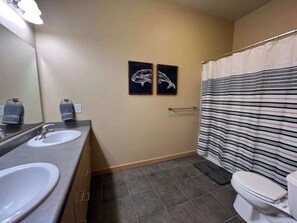 A bathroom with two sinks, a toilet, a shower curtain, and two framed wall art pieces.