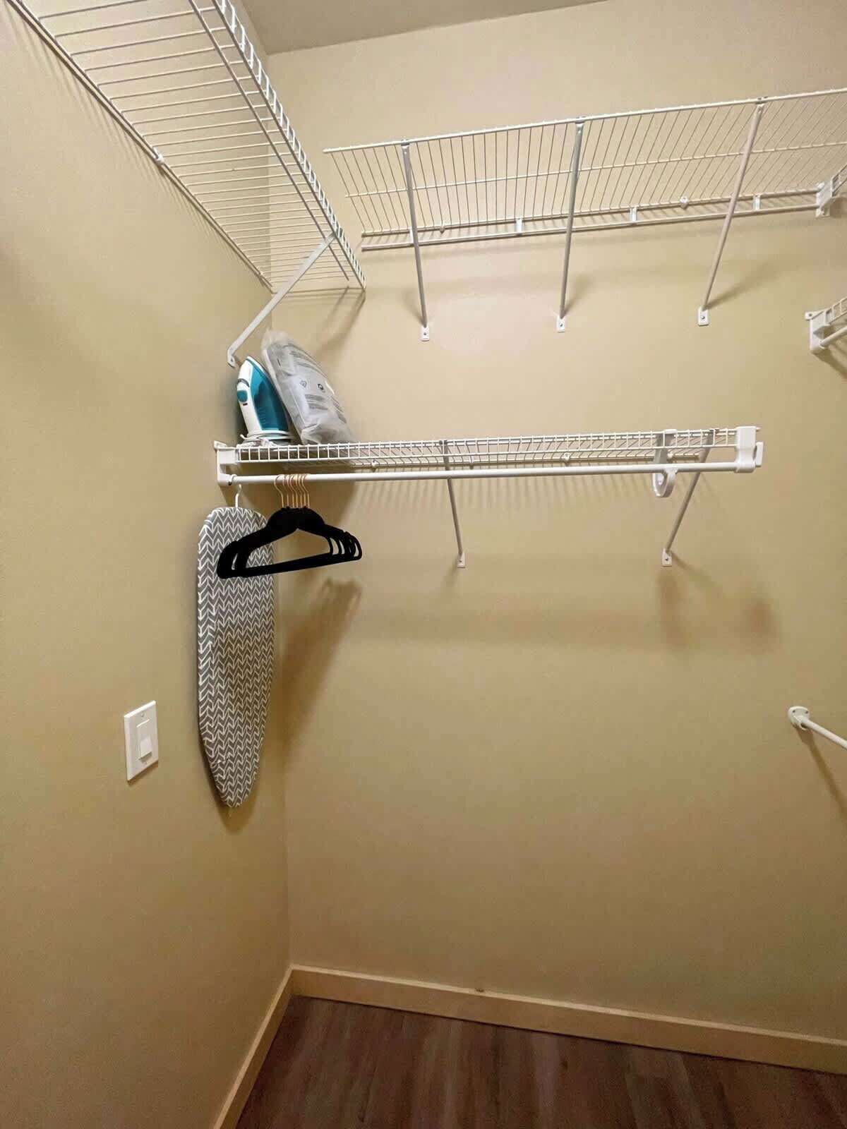 Un armario con varios estantes, una barra para colgar ropa y una plancha pequeña.