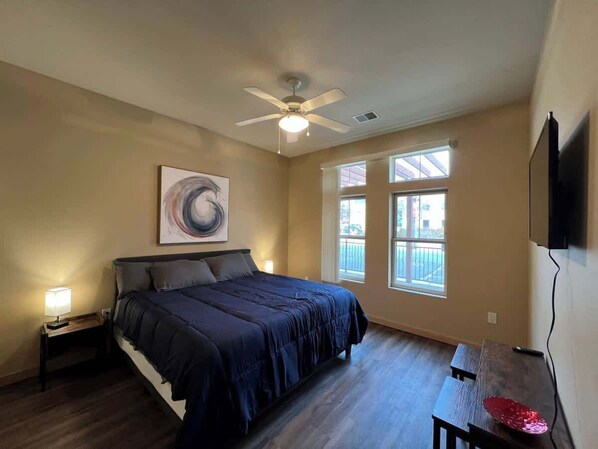 Une chambre à coucher avec un lit, un ventilateur de plafond, une fenêtre et un téléviseur fixé au mur.